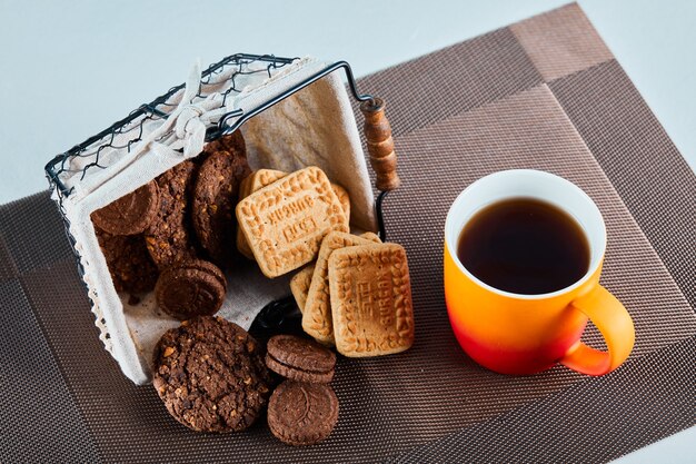Biscotti assortiti, caramelle e una tazza di tè sulla superficie grigia.
