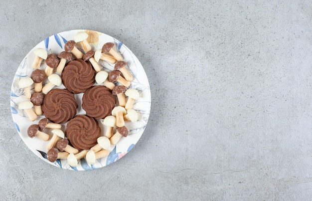 Biscotti circondati da funghi al cioccolato su un piatto su fondo marmo.