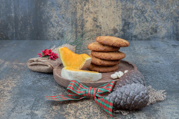 Biscotti con pigne e due fette di zucca su piatto di legno.