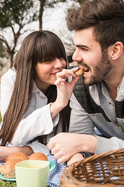 Biscotti d&#39;alimentazione della giovane donna al suo ragazzo al picnic