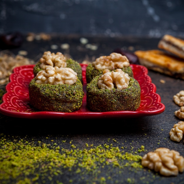 Biscotti del pistacchio di vista laterale in piatto rosso su fondo nero.