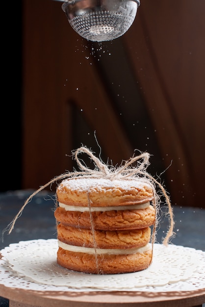 Biscotti deliziosi del panino di vista frontale legati yummy che ottengono polvere di zucchero sulla torta blu scuro della scrivania