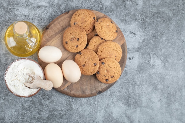 Biscotti di farina d'avena con gocce di cioccolato su una tavola di legno con ingredienti intorno