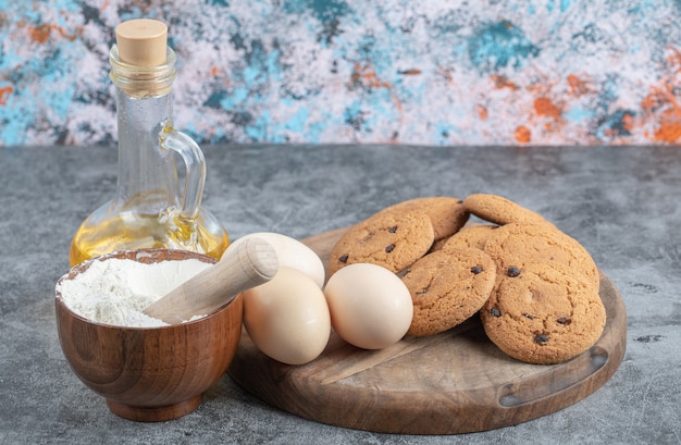 Biscotti di farina d'avena con gocce di cioccolato su una tavola di legno con ingredienti intorno