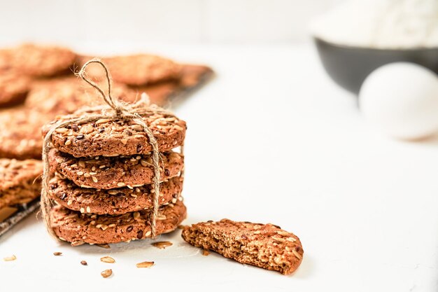 Biscotti di farina d'avena con semi di lino e sesamo su uno sfondo bianco. Uova, farina - ingredienti per fare i biscotti, ricetta di cottura. Messa a fuoco selettiva su biscotti al forno, colazione sana. Prodotti da forno delle feste