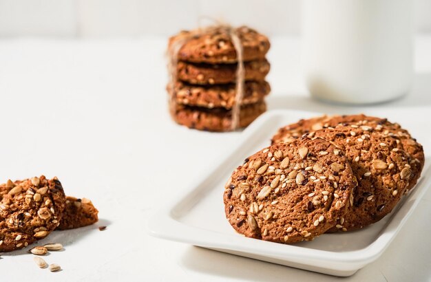 Biscotti di farina d'avena fatti in casa, messa a fuoco selettiva. Biscotti e latte artigianali per la colazione. Biscotti artigianali con semi di lino e sesamo su un piatto bianco. Prodotti da forno delle feste