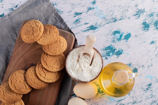 Biscotti di farina d'avena in un piatto di legno con ingredienti intorno.