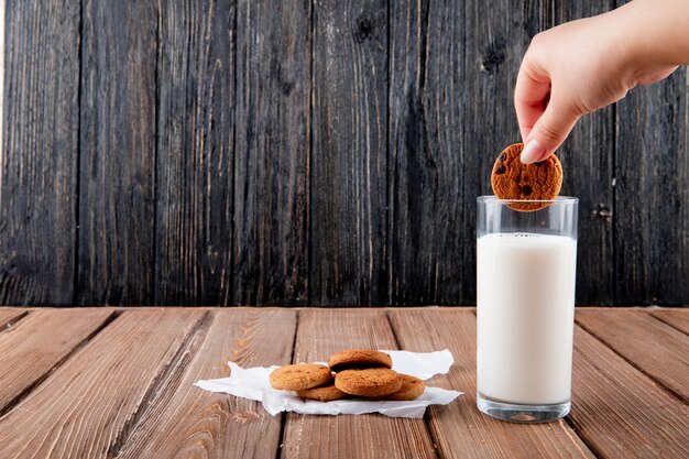 Biscotti di farina d'avena inzuppati della donna di vista frontale su carta da lucido con bicchiere di latte su un fondo di legno