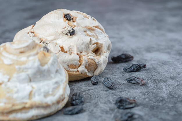 Biscotti di meringa bianca con uvetta nera su una superficie di cemento.