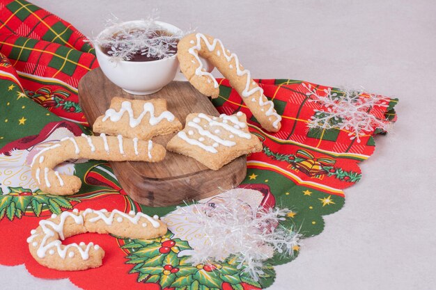 Biscotti di Natale con tè aromatico in tazza sul tavolo bianco.