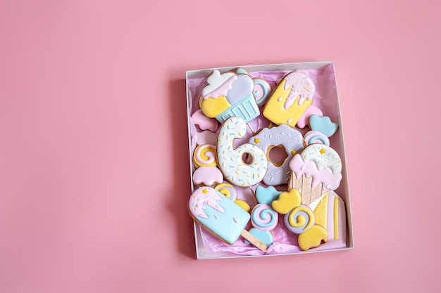 Biscotti di pan di zenzero festivi colorati di diverse forme ricoperti di glassa su sfondo rosa.