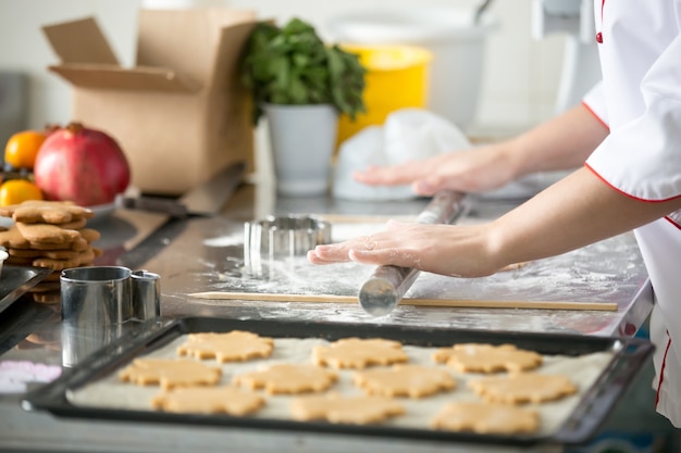 Biscotti di pan di zenzero in un vassoio, pasta di rotolamento delle mani femminili