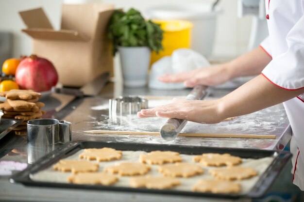 Biscotti di pan di zenzero in un vassoio, pasta di rotolamento delle mani femminili