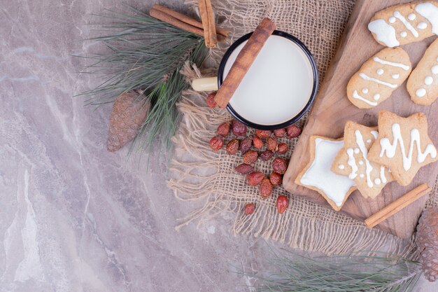 Biscotti di panpepato stella e ovale su una tavola di legno con cannella e una tazza di latte