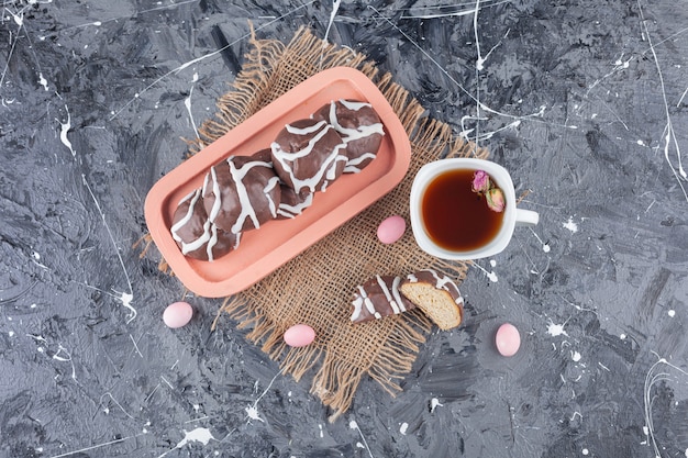 Biscotti di pasta frolla ricoperti di cioccolato bianco e fondente con una tazza di tè in vetro.