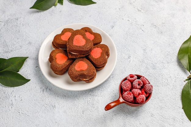 Biscotti di San Valentino a forma di cuore con lamponi congelati su sfondo chiaro