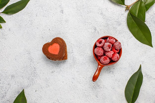 Biscotti di San Valentino a forma di cuore con lamponi congelati su sfondo chiaro