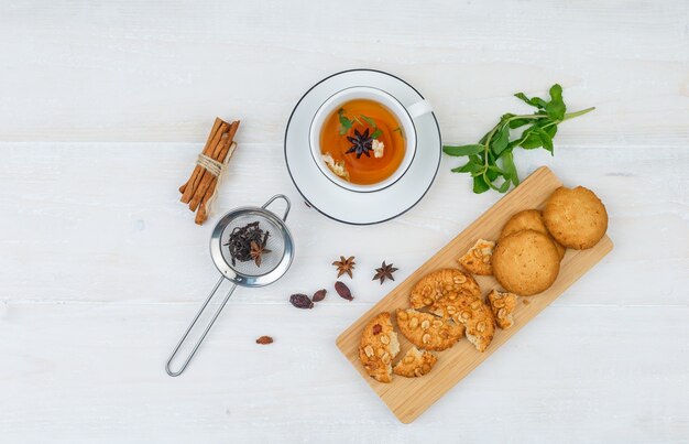 Biscotti di vista dall'alto sul tagliere con tisane, colino da tè e spezie su superficie bianca