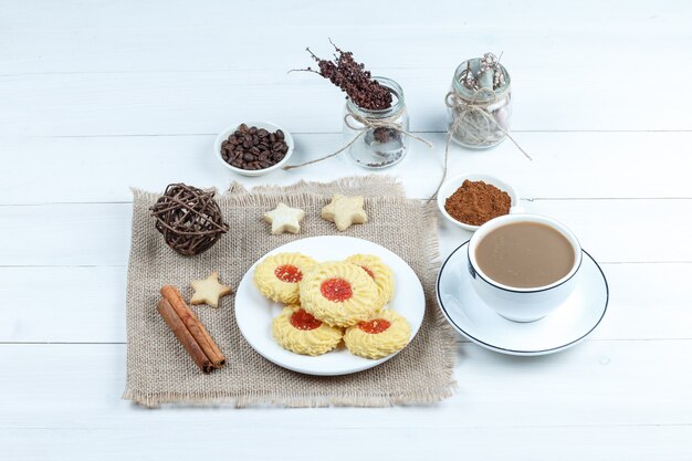 Biscotti di vista di alto angolo, cannella, corde sul pezzo di sacco con una ciotola di caffè istantaneo, tazza di caffè sul fondo del bordo di legno bianco. orizzontale