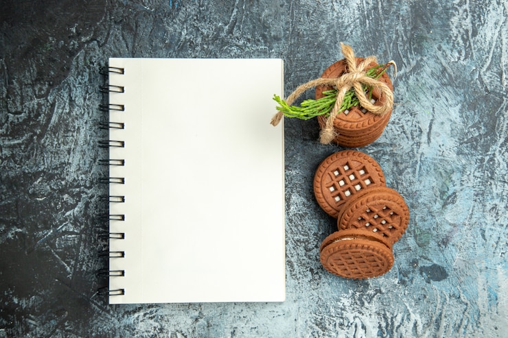 Foto gratuito biscotti di vista superiore con crema legata con il blocco note dei biscotti delle corde sulla superficie grigia