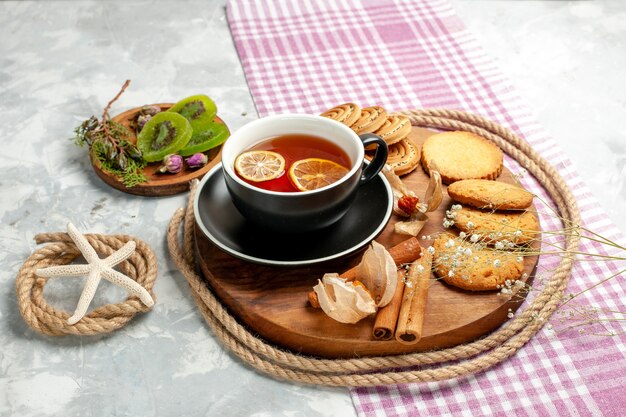 Biscotti di zucchero di vista frontale con la tazza di tè sulla torta dolce della torta del biscotto del biscotto del pavimento bianco