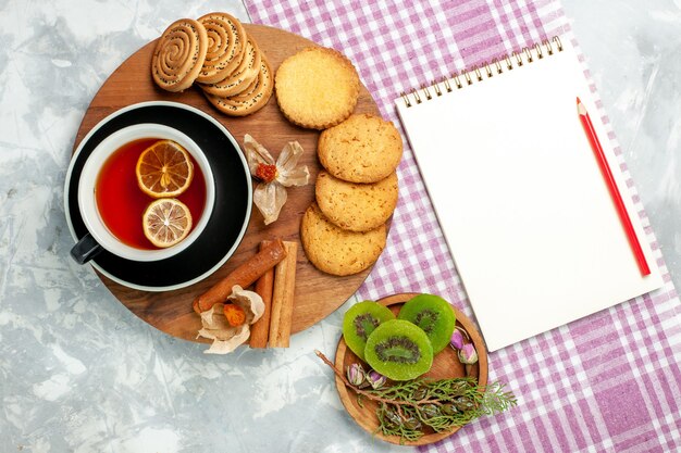 Biscotti di zucchero di vista superiore con la tazza di tè e le fette del kiwi su una torta dolce della torta del biscotto dei biscotti della scrivania bianca