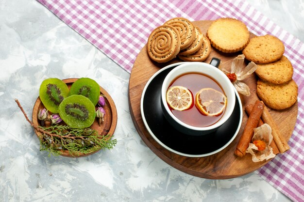 Biscotti di zucchero di vista superiore con la tazza di tè e le fette del kiwi sulla torta dolce del biscotto dei biscotti di superficie bianca chiara