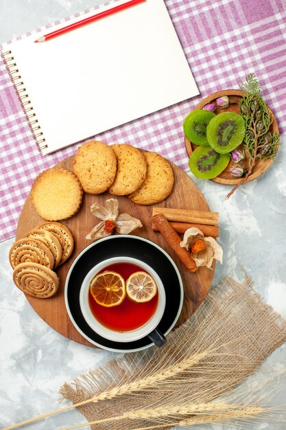 Biscotti di zucchero di vista superiore con la tazza di tè e le fette del kiwi sulla torta dolce del biscotto dei biscotti di superficie bianca chiara