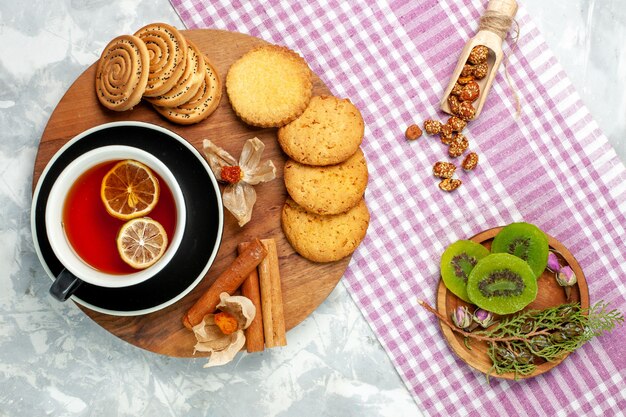 Biscotti di zucchero di vista superiore con la tazza di tè e le fette del kiwi sulla torta dolce della torta del biscotto dei biscotti della parete bianca