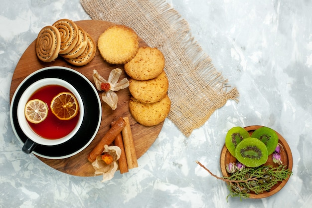 Biscotti di zucchero di vista superiore con la tazza di tè e le fette del kiwi sulla torta dolce della torta del biscotto del biscotto della parete bianca