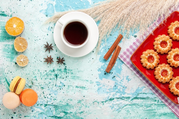 Biscotti di zucchero vista dall'alto all'interno del piatto rosso con una tazza di tè e macarons su sfondo blu