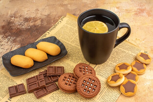 Biscotti diversi e tè in una tazza nera e taccuino sulla tabella di colori misti