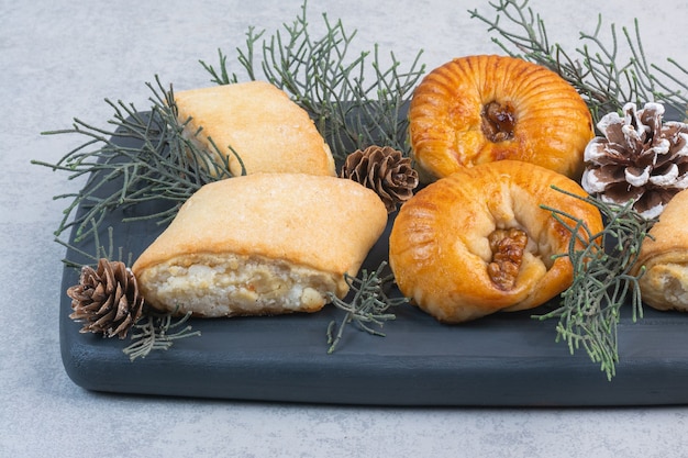 Biscotti diversi, pigna e ramo di pino su un vassoio di legno, sul marmo.