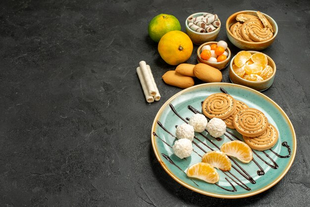 Biscotti dolci di vista frontale con caramelle e mandarini sulla caramella della torta del biscotto della tavola grigia