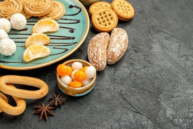 Biscotti dolci di vista frontale con frutta e caramelle sul dolce del biscotto dei biscotti della tavola scura