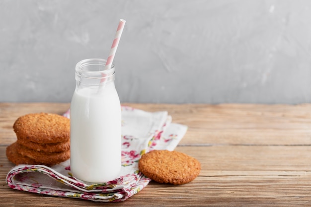 Biscotti e bottiglia per il latte dell'angolo alto con paglia sulla tavola