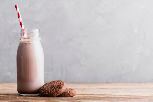 Biscotti e latte al cioccolato di vista frontale in bottiglia con paglia sulla tavola