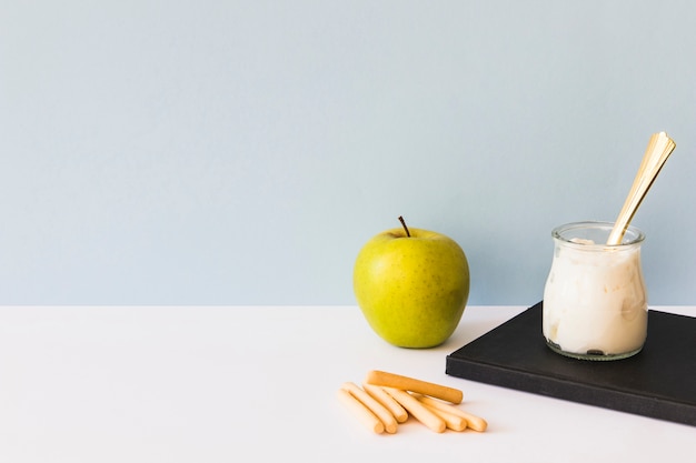 Biscotti e mela vicino a yogurt e notebook