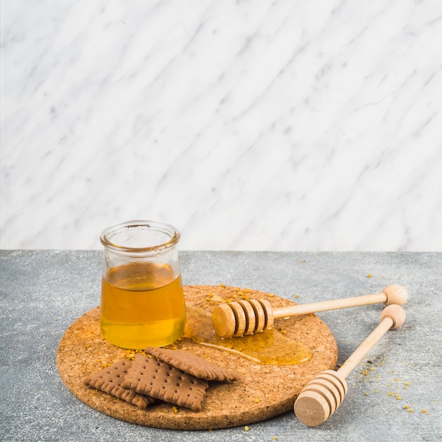 Biscotti e vasetto di miele con mestolo in legno su sottobicchiere di sughero