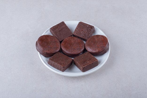 Biscotti e wafer ricoperti di cioccolato su piastra su tavolo di marmo.