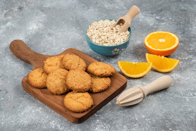 Biscotti fatti in casa su tavola di legno e farina d'avena con arance su superficie grigia.