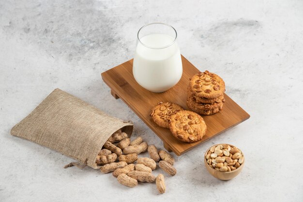 Biscotti gustosi con miele e arachidi e bicchiere di latte su tavola di legno.