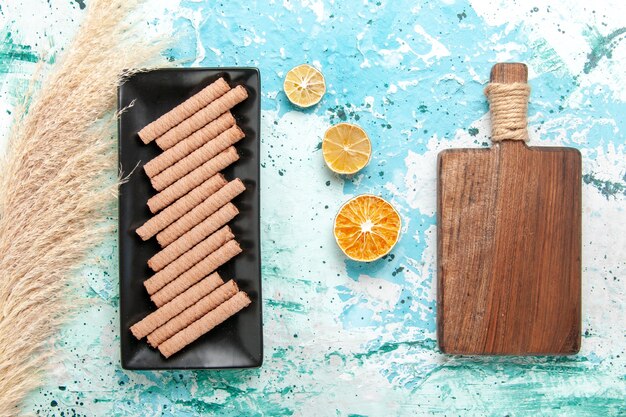 Biscotti lunghi dolci di vista superiore all'interno della tortiera nera sulla torta della torta del tè dello zucchero dolce del biscotto della scrivania blu