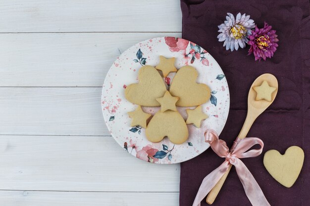 Biscotti piatti laici nel piatto e cucchiaio di legno con fiori su fondo in legno e tessile. orizzontale