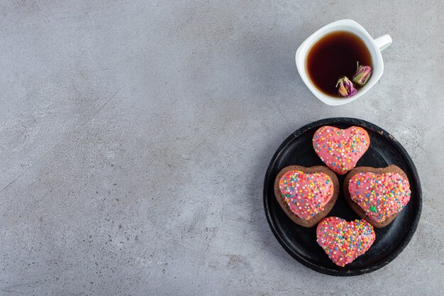 Biscotti rosa in forma sentita con tè su sfondo grigio.