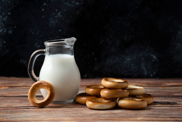 Biscotti rotondi e brocca di vetro di latte sulla tavola di legno.