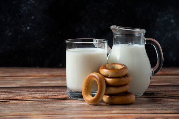 Biscotti rotondi, tazza di vetro e brocca di latte sulla tavola di legno.