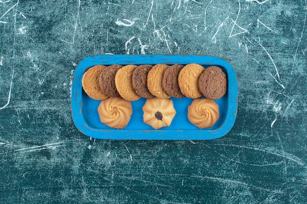 Biscotti semplici e al cioccolato su un vassoio di legno, sullo sfondo blu. Foto di alta qualità