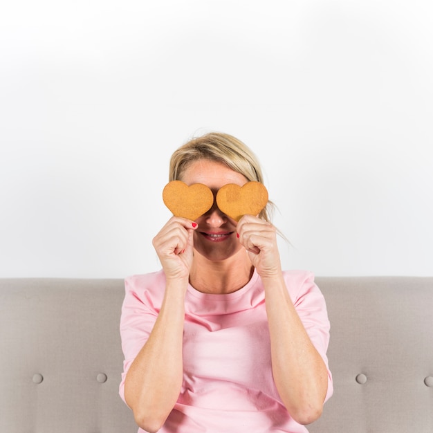 Biscotti sorridenti di forma del cuore della tenuta della donna lei occhi contro il contesto bianco