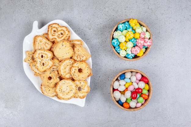 Biscotti su un piatto decorato accanto a ciotole di caramelle sulla superficie di marmo.